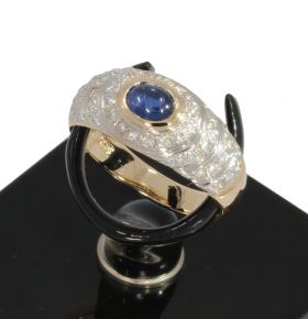 14 karaats geelgouden design ring met een centrale cabochon geslepen saffier omlijst door 46 briljant geslepen diamanten(totaal ca. 0,25ct). De ringmaat is 16/16,25, breedte ringkop 8mm, gewicht 3,50 gram. Conditie uitmuntend, gestempeld met het 585 goudm