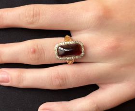 15 karaats gouden ring met een cabochon geslepen (vermoedelijke) wijnrode granaat omlijst door 32 diamanten, handgemaakt juweel. De ringmaat is 17,5(55), afmetingen ringkop 20x13mm, gewicht 5 gram. Conditie fraai, gestempeld met het 15 karaats goudmerk 62
