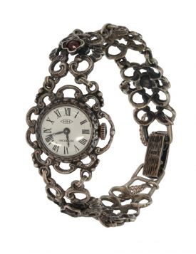 Vintage zilveren damespolshorloge aan ajourbewerkte zilveren band met bloemschakels waarin granaat edelsteen. Draaglengte van dit sieraad is ca. 17cm, doorsnee klok 24mm, breedte band 17mm, totaalgewicht 26 gram. Merk HH, uurwerk en band gestempeld met he